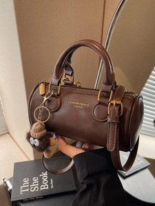 Dark brown cylindrical Boston bag with top handles, adjustable strap and plush pendant