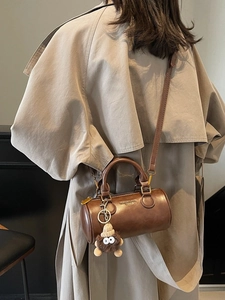 Dark brown leather barrel bag with plush monster charm and adjustable shoulder strap