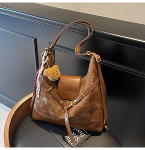 Detailed view of a brown suede hobo bag with teddy charm and silk scarf on a black chair