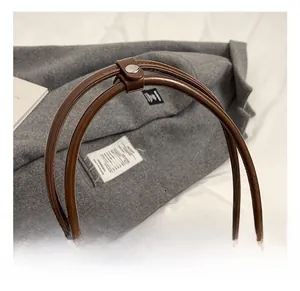Detailed close-up of brown leather handbag dual handles with silver metal buckle strap