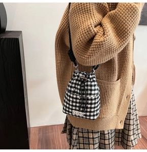 Λεπτομέρεια ασπρόμαυρης τσάντας bucket gingham με μεταλλικά τρουκ και κορδόνι
