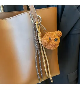 Detail eines Plüschbären-Anhängers mit gewebten Quasten an einer braunen Ledertasche
