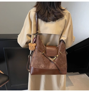Detail of dark brown leather tote featuring suede panels and a plush bear pendant