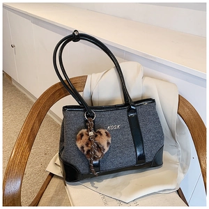 Detail of grey fabric tote bag with black patent leather trim and plush leopard heart charm