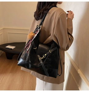 Detail of suede tote bag with golden buckle, plush bear charm and leather stitching