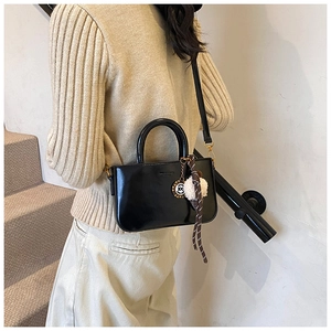 Détail d'un mini sac bandoulière noir brillant avec pompon décoratif et poignée