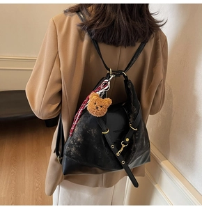 Detail of black suede tote bag with gold hardware and a cute plush bear charm