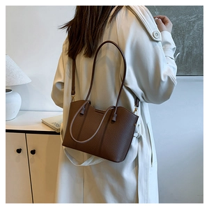 Détail du sac cabas en cuir grainé marron foncé porté sur un manteau long blanc