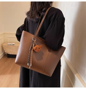 Détail d'un sac cabas marron avec un pendentif ours en peluche et un cordon tressé