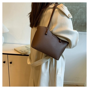Sac fourre-tout en cuir litchi marron porté avec un manteau beige élégant de ville