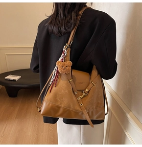 Detail of tan leather tote bag with teddy charm and decorative scarf on model