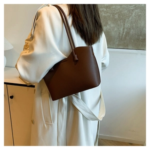 Détail du sac à bandoulière en cuir grainé marron foncé porté sur un manteau beige