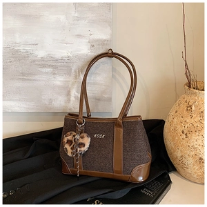 Detail of a brown large tote bag with a leopard print heart charm and metal logo