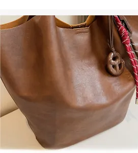 Gros plan sur un sac cabas en cuir marron avec corde tressée et charm en forme de bretzel