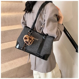 Detail view of large grey tote bag with black patent leather handles and leopard heart charm