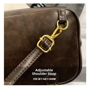 Detailed close-up of adjustable shoulder strap with gold metal hooks on brown leather bag