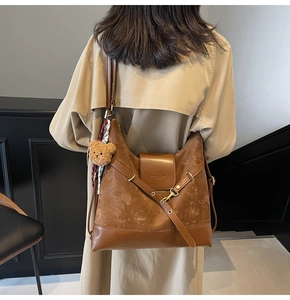 Detailed view of brown suede tote bag with plush bear charm and adjustable shoulder strap