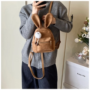 Détail d'un mini sac à dos en daim marron avec oreilles de lapin et charme monstre blanc