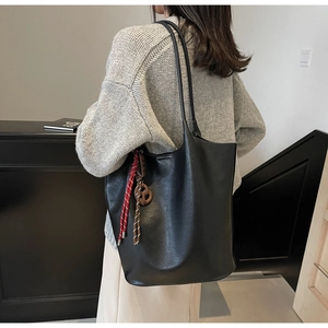 Détail du sac cabas noir en similicuir avec pendentif tressé porté par un mannequin