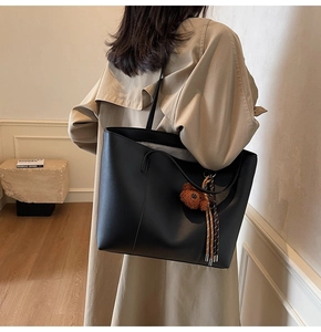 Détail d'un sac cabas noir minimaliste orné d'un ours en peluche et de pompons à franges