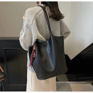 Détail latéral du grand sac cabas noir en cuir avec pendentif tressé sur la bandoulière