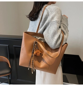 Detail der camel-farbenen Tote-Tasche mit Plüschbären-Anhänger und Quaste am Trageriemen