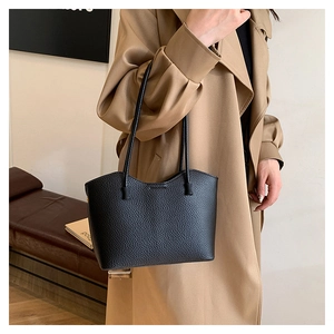 Vue détaillée d'un grand sac cabas en cuir grainé noir porté avec un manteau beige chic