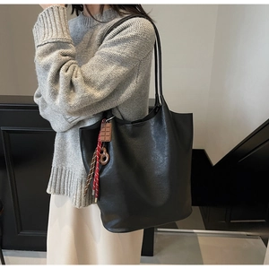 Détail du sac seau en cuir noir avec breloques chocolat et donut sur la bandoulière