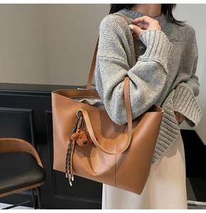 Détail d'un sac cabas en cuir marron avec pompon tressé et un petit charm d'ours