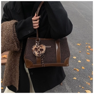 Detail view of brown patchwork tote bag with tweed texture and heart leopard charm