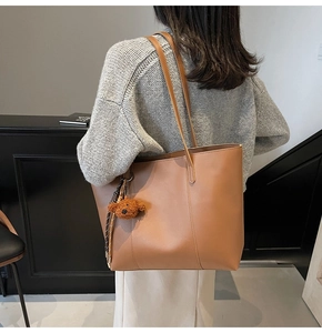 Détail d'un sac cabas en cuir marron avec un pendentif ours en peluche et surpiqûres verticales