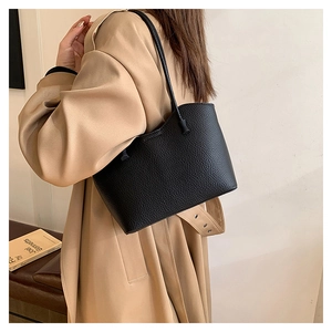 Détail d'un sac cabas en cuir grainé noir porté avec un trench-coat minimaliste chic