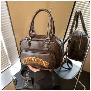 Detailed close-up of brown PU leather Boston bag with plush holiday lettering and gold zipper
