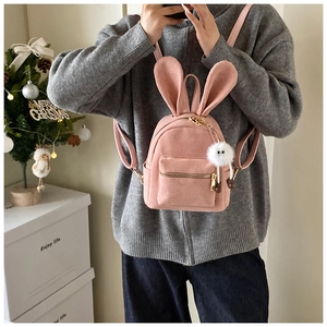 Détail d'un sac à dos en velours rose avec oreilles de lapin et pompon en peluche blanc