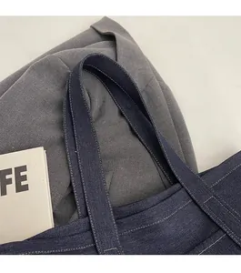 Detail of wide reinforced denim shoulder strap with precision stitching on blue tote bag