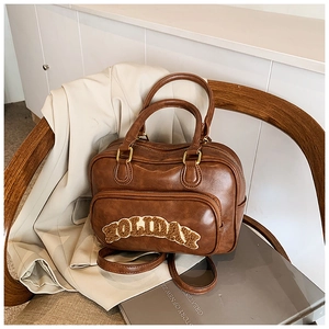 Close-up of vintage brown leather bag with HOLIDAY embroidery on a wooden chair