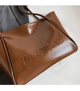 Dettaglio della borsa tote in pelle marrone lucida con lettere a rilievo e tracolla sottile