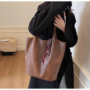 Détail d'un grand sac cabas en cuir marron avec un pendentif chocolat et cordon tressé décoratif