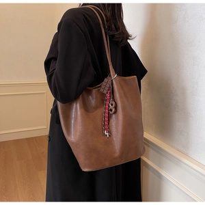 Détail d'un grand sac fourre-tout marron foncé avec charme chocolat porté par un modèle