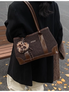 Brown tweed tote bag with leather trim and leopard heart charm on a black coat