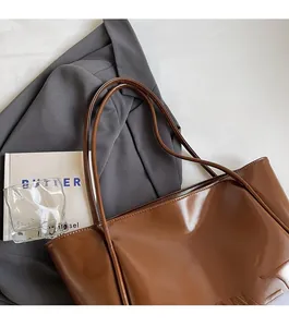 Dettaglio ravvicinato della borsa tote marrone lucida con scritte impresse e spalline sottili