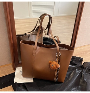 Détail du sac fourre-tout en cuir caramel avec breloque ours et pompon tressé décoratif