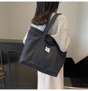 Detail shot of a large dark blue denim tote bag with contrast stitching and pocket tag