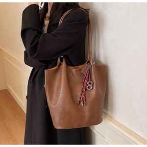 Détail d'un grand sac cabas en cuir marron avec un charme chocolat sur l'épaule du modèle
