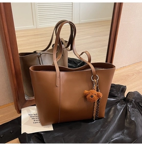 Détail d'un cabas en cuir marron foncé avec breloque ours en peluche sur tissu noir