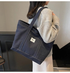 Detailed shot of large dark blue denim tote bag with brand logo patch and wide strap