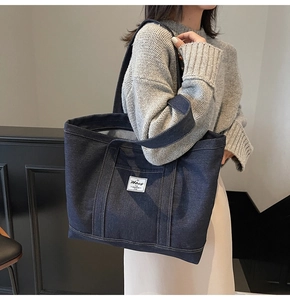 Detail of dark blue denim tote bag with striped lining and white logo patch