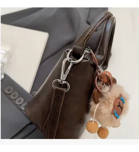 Detail of dark brown matte handbag with silver metal buckle and plush pom-pom charm