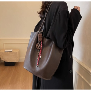 Détail du sac seau en cuir marron foncé avec pendentif chocolat porté par un mannequin