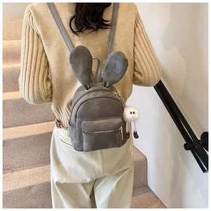 Détail d'un mini sac à dos gris avec des oreilles de lapin et un pendentif pompon mignon